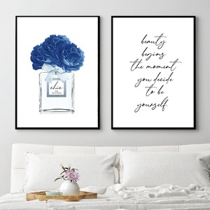 Op de afbeelding: Twee ingelijste prints, een met een blauwe bloemillustratie van een parfumfles met het woord "chic" op het etiket, en de andere met de tekst "schoonheid begint op het moment dat je besluit om jezelf te zijn."