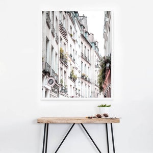 May include: A black and white photograph of a narrow street in Paris, France. The street is lined with tall, white buildings with balconies and windows. The buildings are in focus, while the street is blurred in the background.
