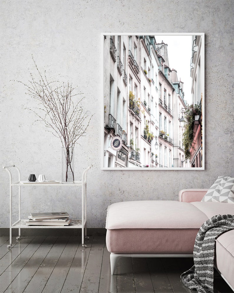 May include: A black and white photograph of a narrow street in Paris, France. The street is lined with tall buildings with balconies and windows. The buildings are painted in shades of white and gray. The street is empty except for a few streetlights.