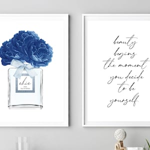 Op de afbeelding: Twee ingelijste prints, een met een blauwe bloemillustratie van een parfumfles met het woord "chic" op het etiket, en de andere met een zwart-wit citaat dat luidt "schoonheid begint op het moment dat je besluit jezelf te zijn."