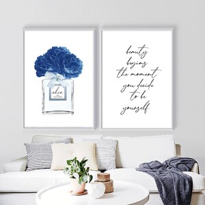Op de afbeelding: Twee ingelijste prints met witte achtergronden. De linker print toont een blauwe aquarel-illustratie van een parfumfles met een blauwe bloem erop. De rechter print toont de tekst "schoonheid begint op het moment dat je besluit om jezelf te zijn."