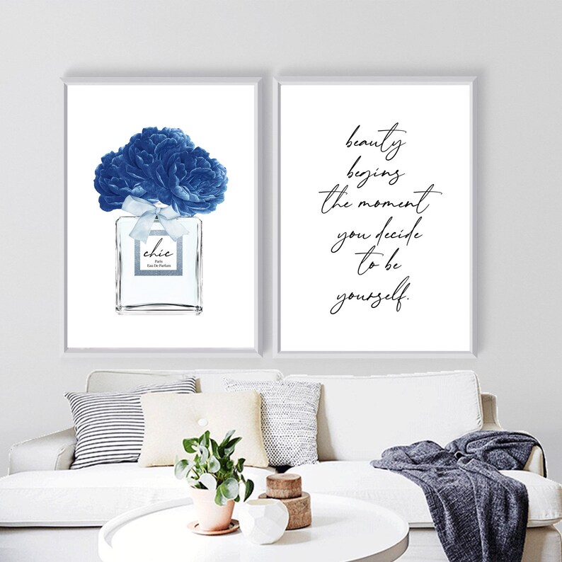 Op de afbeelding: Twee ingelijste prints met witte achtergronden. De linker print toont een blauwe aquarel-illustratie van een parfumfles met een blauwe bloem erop. De rechter print toont de tekst "schoonheid begint op het moment dat je besluit om jezelf te zijn."