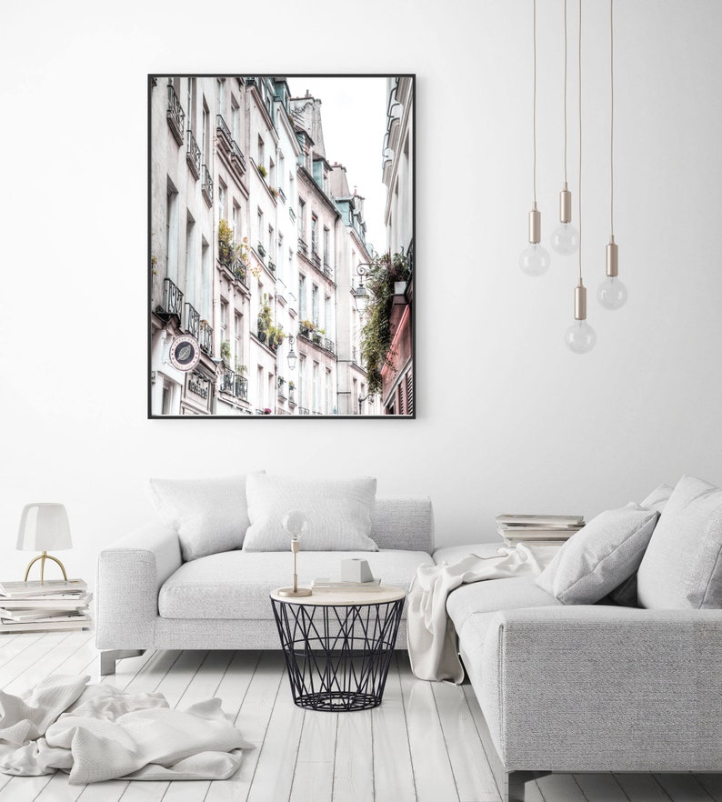 May include: A photograph of a narrow street in Paris, France. The street is lined with tall, white buildings with balconies and windows. The buildings are in a row, and the street is narrow, with a few people walking on the sidewalk.