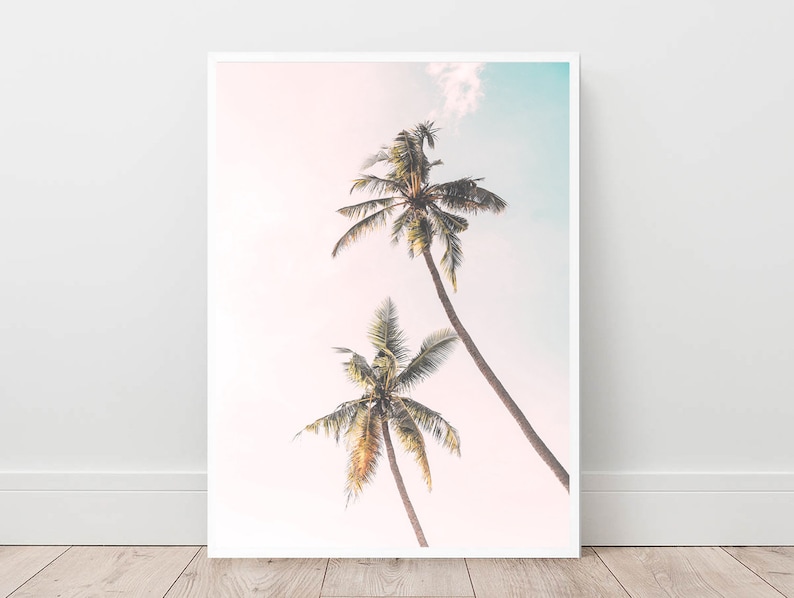 May include: Two palm trees with green fronds against a soft pink and blue sky. The sky is slightly cloudy.