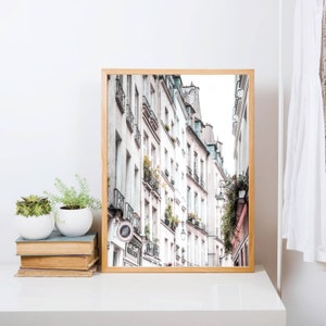 May include: A framed photograph of a narrow street in Paris, France. The street is lined with tall, white buildings with balconies and windows. The buildings are in a faded, vintage style.
