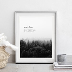 May include: A black and white print of a forest with fog. The print is framed in a white frame and has the word "wanderlust" and its definition printed below the image.