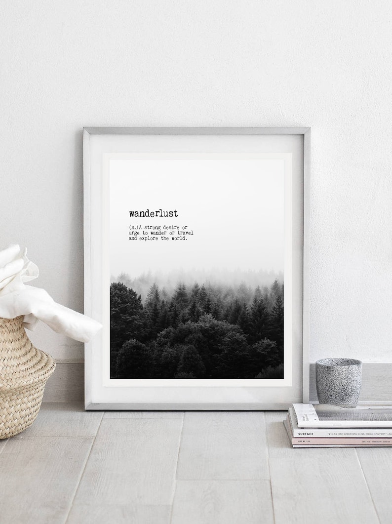 May include: A black and white print of a forest with fog. The print is framed in a white frame and has the word "wanderlust" and its definition printed below the image.