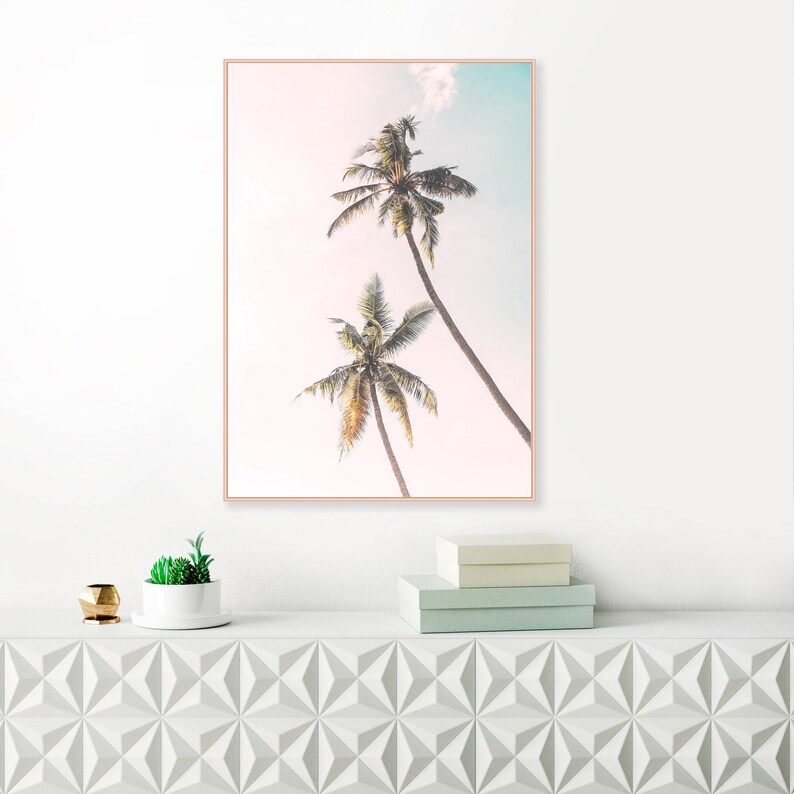 May include: A framed print of two palm trees against a soft pink and blue sky. The print has a light, airy feel and would be a great addition to a beach-themed home.