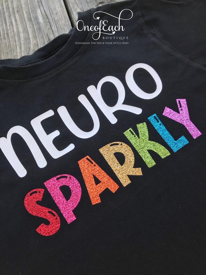 May include: Black t-shirt with the words "Neuro Sparkly" in white and rainbow glitter lettering.