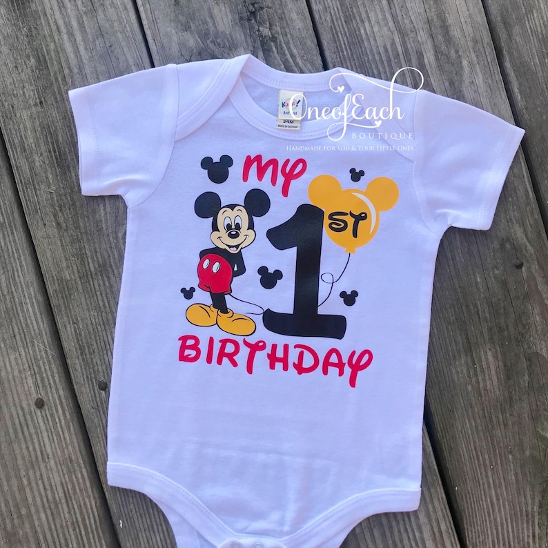 May include: White onesie featuring a black and red Mickey Mouse character holding a yellow balloon that says "1st". The onesie also says "my 1st birthday" in red and black.