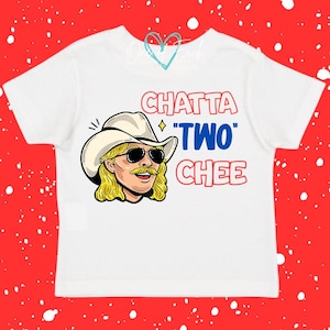 May include: A white short-sleeve t-shirt featuring a graphic illustration of a person with blonde hair, a mustache, and a cowboy hat wearing sunglasses. The text CHATTA "TWO" CHEE is printed in red and blue next to the illustration.