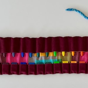 May include: A burgundy velvet crayon roll with a rainbow of crayons and a blue and purple yarn tie.
