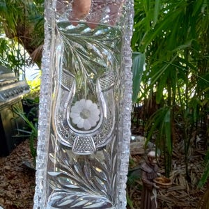 May include: A rectangular clear glass tray featuring a decorative etched horseshoe design with a central flower motif. The tray has a textured, faceted border with a cross-hatched pattern and leaf-like engravings on the interior surface.