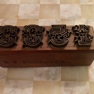 May include: A wooden block with four metal stamps featuring intricate floral designs. The block is labeled "E.B. Erlanger".