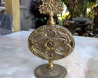 May include: An antique gold-toned perfume bottle with an oval body and a decorative floral design. The bottle has a detailed base and a tree-like stopper. The ornate design features intricate patterns and a vintage aesthetic.