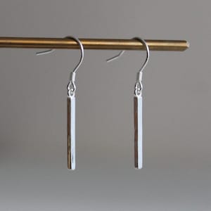 May include: A pair of silver dangle earrings with a long, thin, rectangular bar pendant.