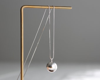 May include: A silver necklace with a large, round pendant hanging from it. The necklace is displayed on a gold stand.