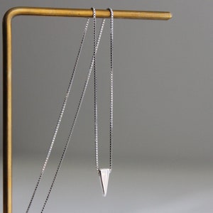 May include: A silver chain necklace with a small triangle pendant.