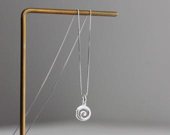 May include: A silver necklace featuring a delicate box chain and a small, circular pendant with an embossed spiral design. The pendant hangs from a simple jump ring, and the entire piece is crafted from a polished, reflective silver metal.