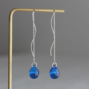 Könnte beinhalten: Ein Paar silberne Ohrringe mit blauen, tropfenförmigen Glasperlen am Ende jeder Kette.