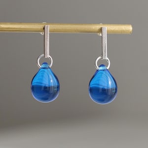 May include: A pair of silver dangle earrings with blue glass teardrop shaped charms.