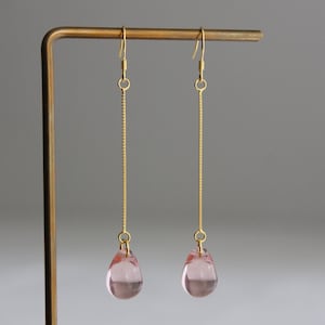 Op de afbeelding: Een paar gouden oorhangers met roze traanvormige glazen kralen.
