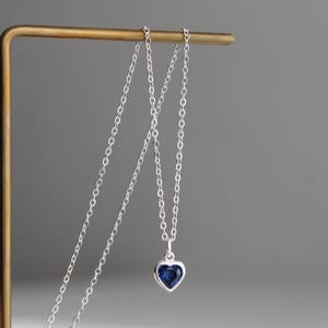 May include: A silver chain necklace with a small heart pendant featuring a blue gemstone.