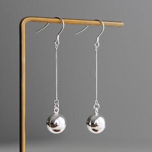 May include: A pair of silver dangle earrings with a round ball charm at the end of each chain.