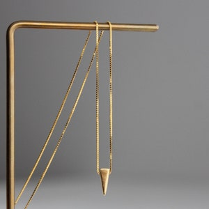 May include: Two gold chains with a small gold triangle pendant hanging from the bottom chain. The chains are displayed on a gold metal stand.