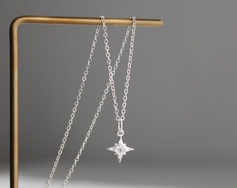 Puede incluir: Un collar de plata con un colgante en forma de estrella. El colgante tiene una piedra transparente en el centro y está rodeado de piedras más pequeñas.
