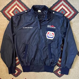 Puede incluir: Una chaqueta azul marino con un logotipo bordado en blanco que dice "The Canadian Tire Dress" y un parche con el texto "Molson Drag Boat Challenge" y un logotipo para "Molson Canadian".