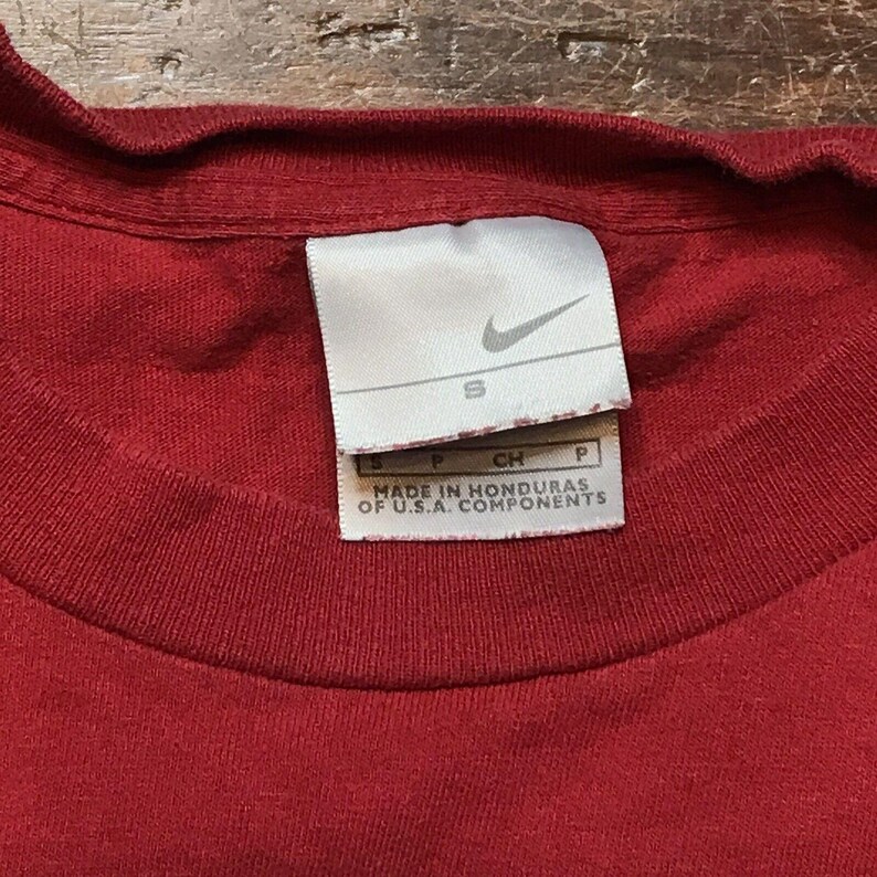 May include: Red t-shirt with a white Nike tag that says "S" and "MADE IN HONDURAS OF U.S.A. COMPONENTS".