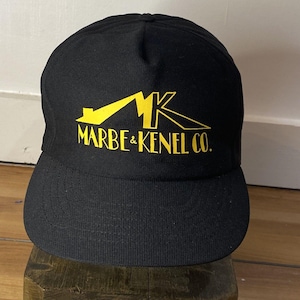May include: Black baseball cap with a yellow logo that says "Marbe & Kenel Co."
