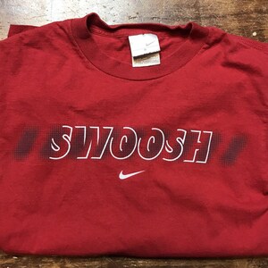 May include: Red t-shirt with a white "SWOOSH" graphic and a white Nike swoosh logo.