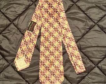 May include: A yellow, brown, and pink patterned silk tie with a "Remarkable" label. The tie has a geometric design with small diamonds and ovals.