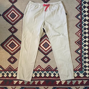 May include: A pair of light beige pants with a drawstring waist and a red drawstring. The pants are made of a soft, comfortable fabric and have a relaxed fit.