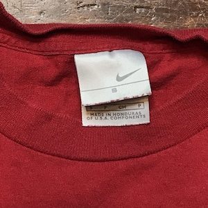 May include: Red t-shirt with a white Nike logo and tag. The tag says "Made in Honduras of U.S.A. components" and has a size "S" printed on it.