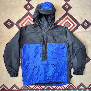 Op de afbeelding: Een zwart en blauw hooded jack met een ritssluiting en een kangoeroezak. Het jack heeft een capuchon met trekkoord en elastische manchetten.