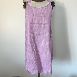 May include: A vintage lavender dress with a white collar and a geometric pattern. The sleeveless dress has a scalloped hem and is displayed on a mannequin. The dress is made of a lightweight fabric.