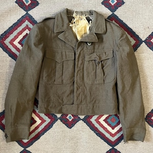 May include: A brown military-style jacket with a button closure and multiple pockets. The jacket has a worn look and is made of a textured fabric.