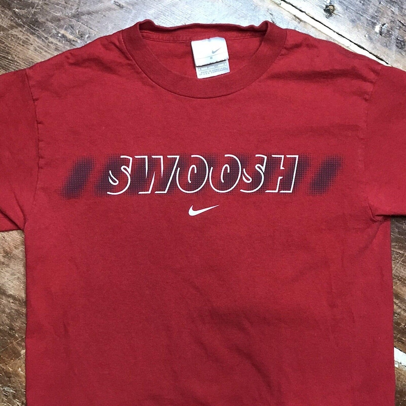 May include: Red t-shirt with a white "SWOOSH" graphic and a white Nike swoosh logo.