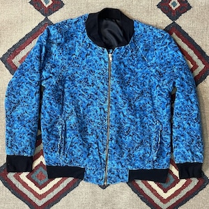 May include: A blue bomber jacket with a black zipper and black ribbed cuffs and waistband. The jacket has a blue and black abstract pattern.