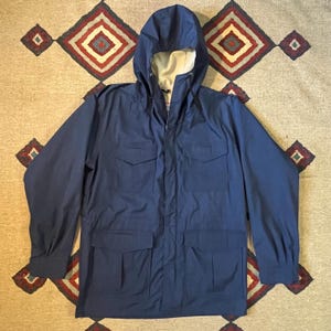 May include: A navy blue hooded jacket with a zipper closure and multiple pockets. The jacket has a fleece lining in the hood.