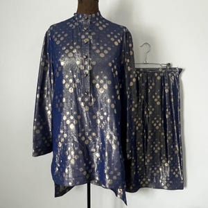 May include: A two-piece outfit consisting of a long-sleeved blouse and a skirt. Both pieces are navy blue with a gold polka dot pattern.