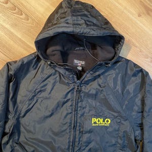May include: Black hooded jacket with a zipper closure and a yellow embroidered logo that reads "POLO JEANS COMPANY".