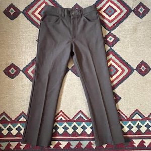May include: Dark gray trousers with a button closure and front pockets. The pants have a classic, straight-leg design. The trousers are displayed on a patterned rug.