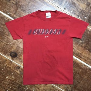 May include: Red t-shirt with a white "SWOOSH" logo and a white Nike swoosh logo.