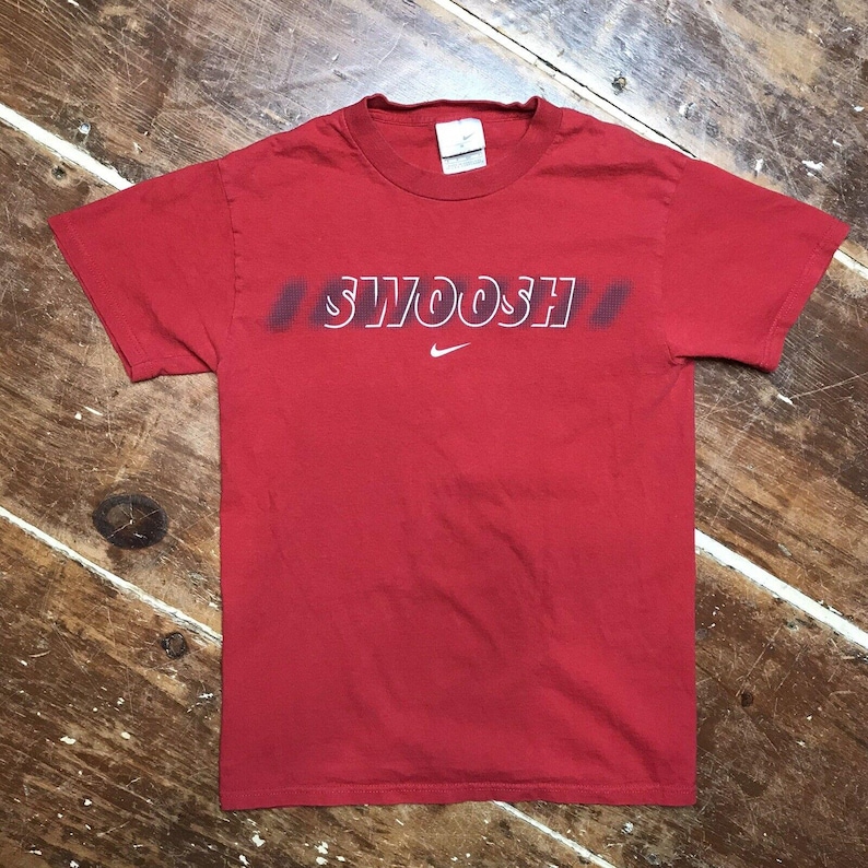 May include: Red t-shirt with a white "SWOOSH" logo and a white Nike swoosh logo.