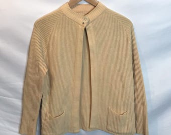 May include: A beige ribbed cardigan with a single button closure and two pockets. The cardigan is open in the front and has a long sleeve.