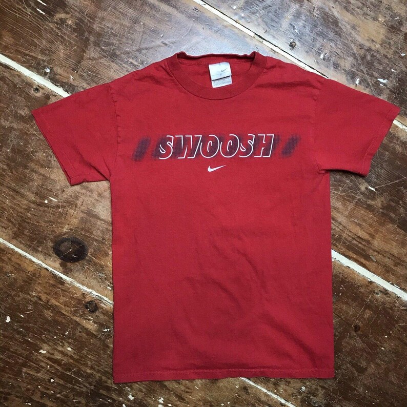 May include: Red short-sleeved t-shirt with a white "SWOOSH" graphic and a white Nike swoosh logo.